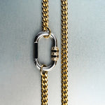 Gold chain necklace with silver carabiner pendant featuring gold lock with diamond detailing on gray background