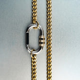 Gold chain necklace with silver carabiner pendant featuring gold lock with diamond detailing on gray background