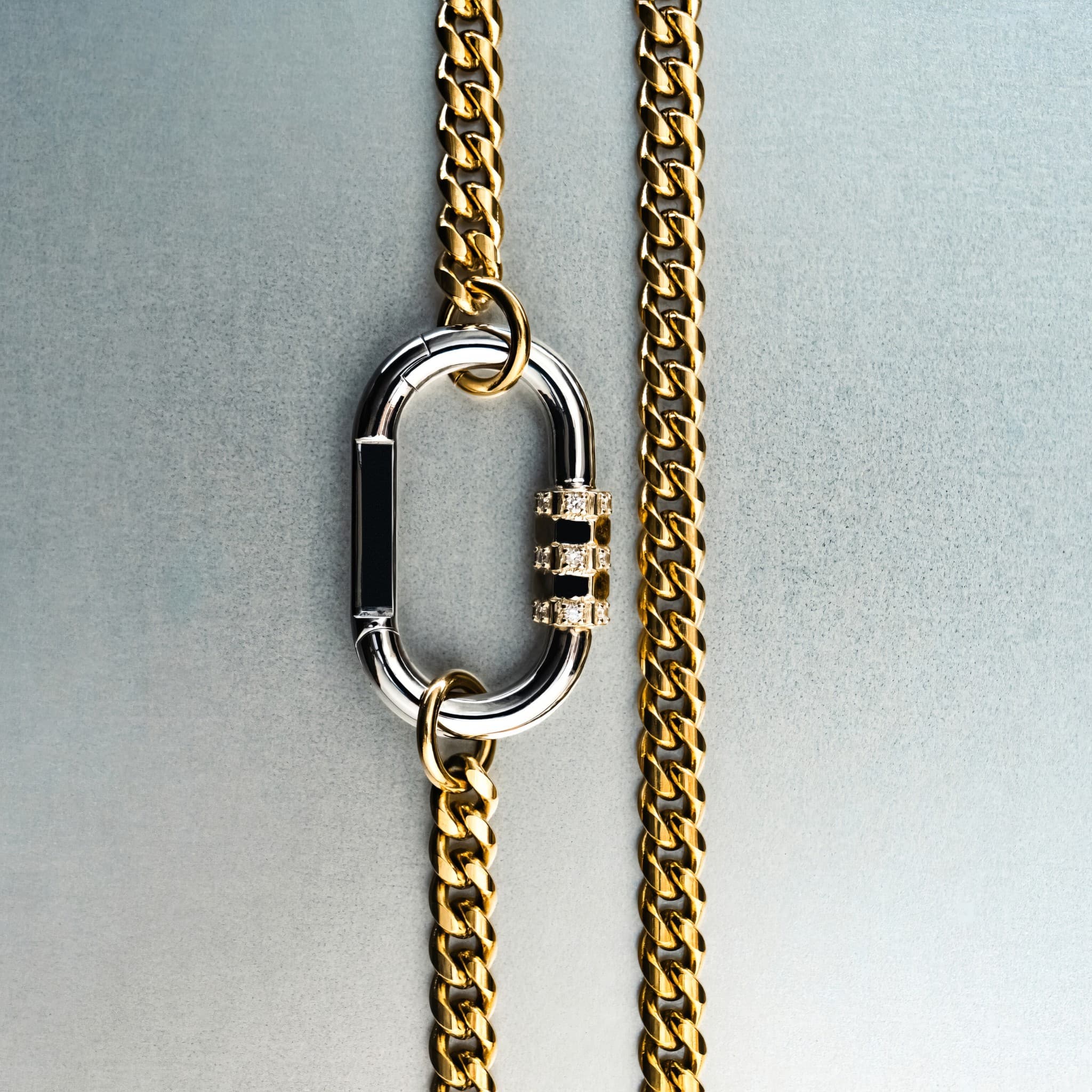Gold chain necklace with silver carabiner pendant featuring gold lock with diamond detailing on gray background