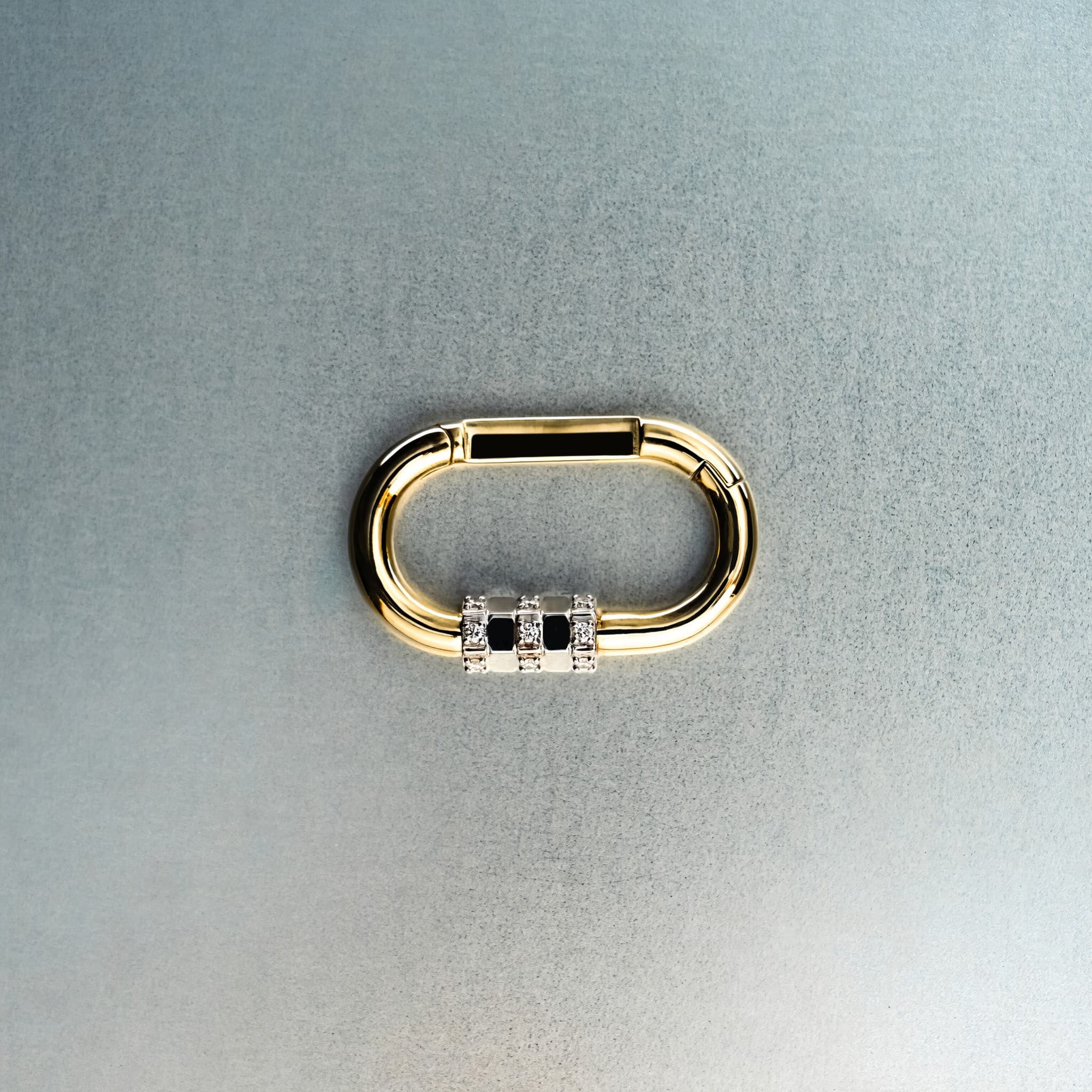 Gold carabiner pendant with diamond-detail lock on light gray background