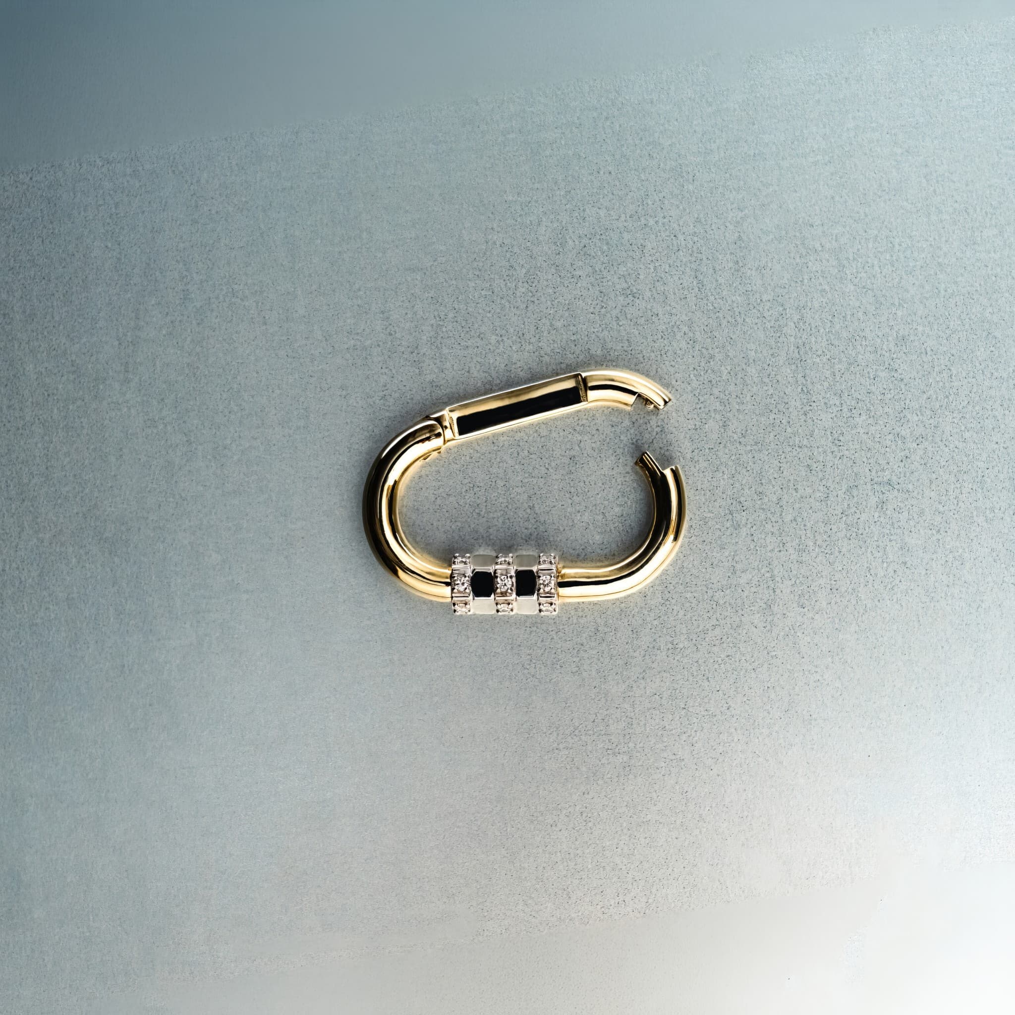 Open gold carabiner pendant featuring diamond lock detail on light gray background