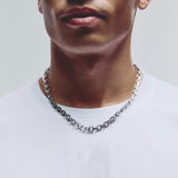 A close-up of a man wearing a silver, chunky washer chain chain necklace with a white crew-neck t-shirt against a light gray background.