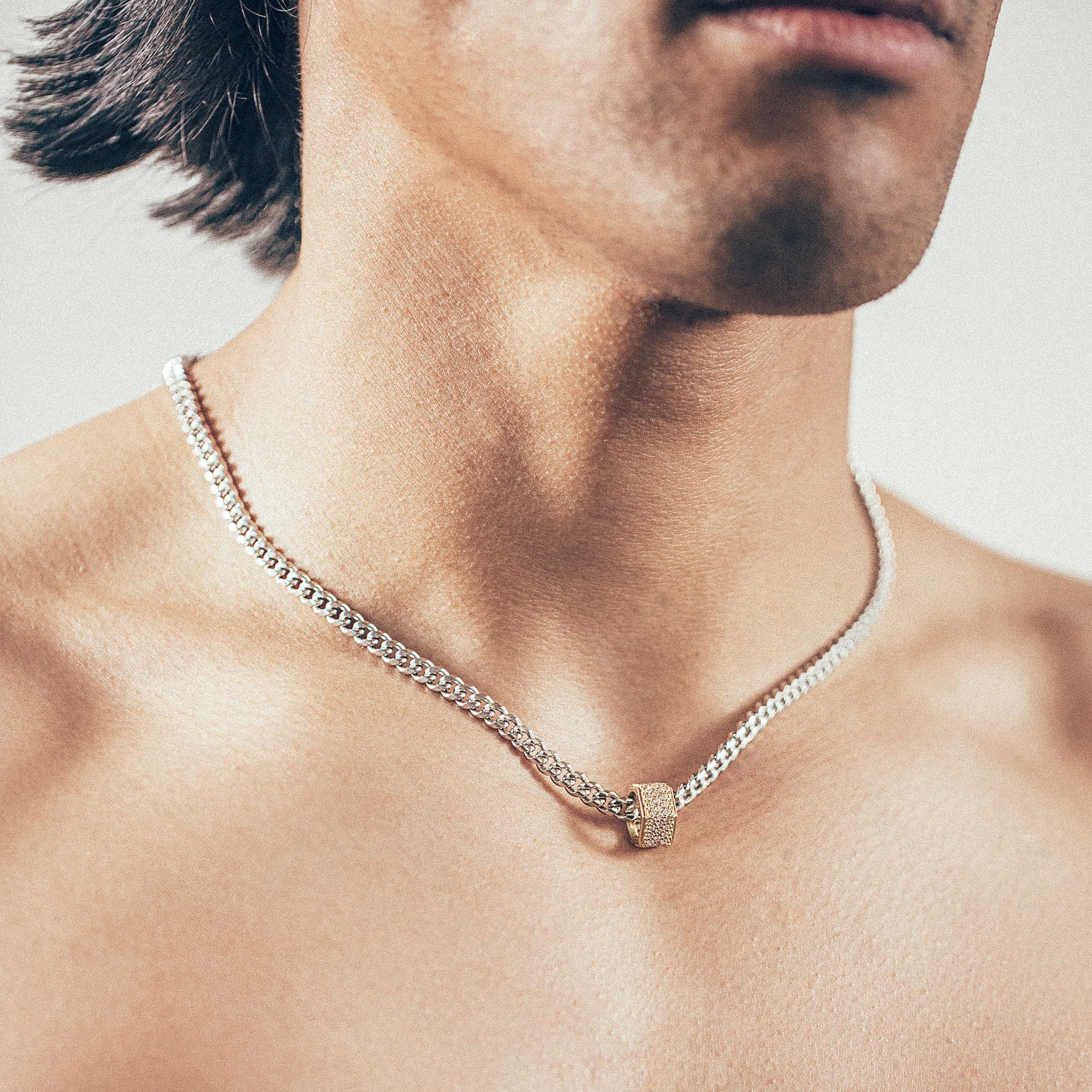 Close-up of person wearing silver chain necklace with gold hex nut bead covered in white diamonds