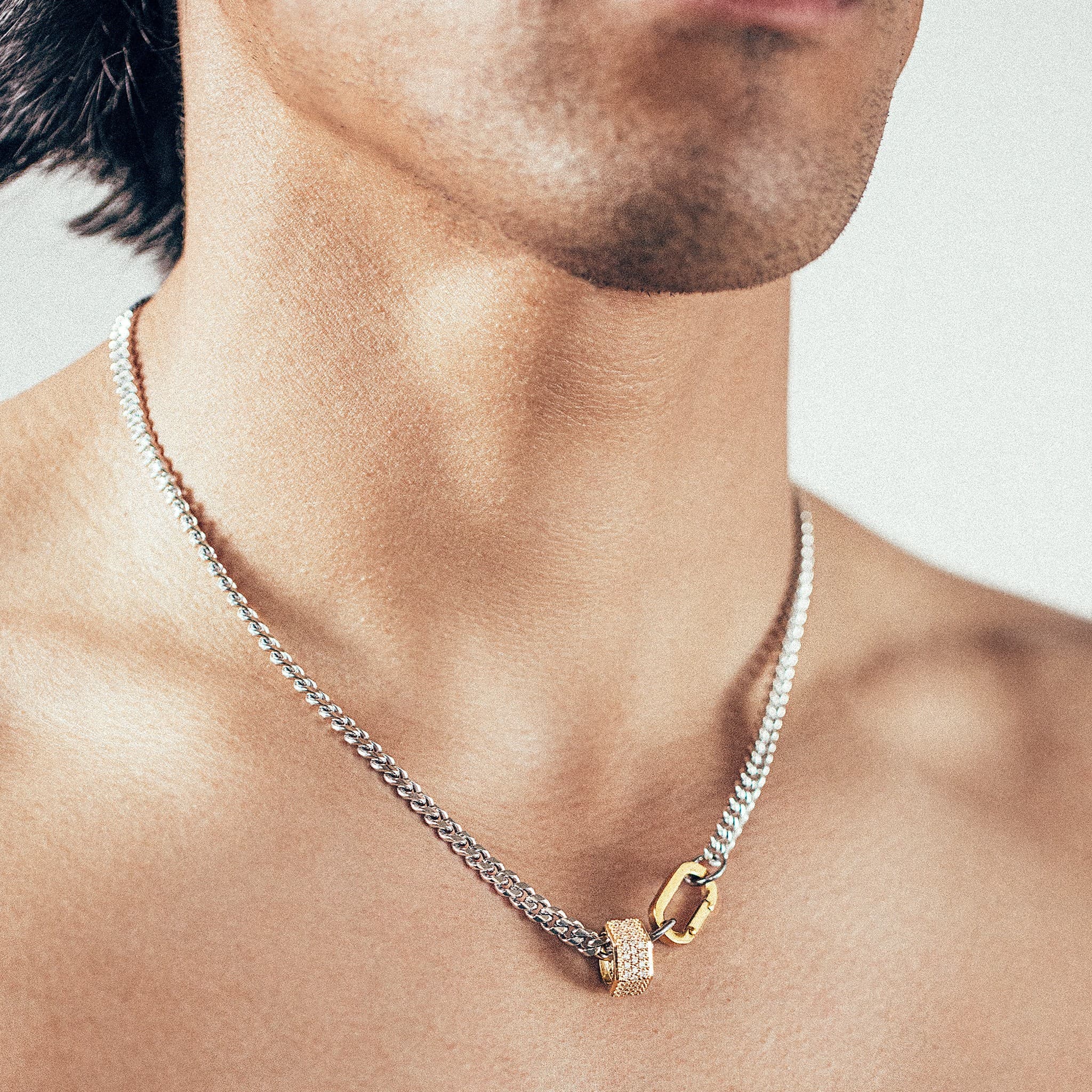 Close-up of person wearing silver chain necklace with gold hex nut bead covered in white diamonds and gold carabiner clasp. 