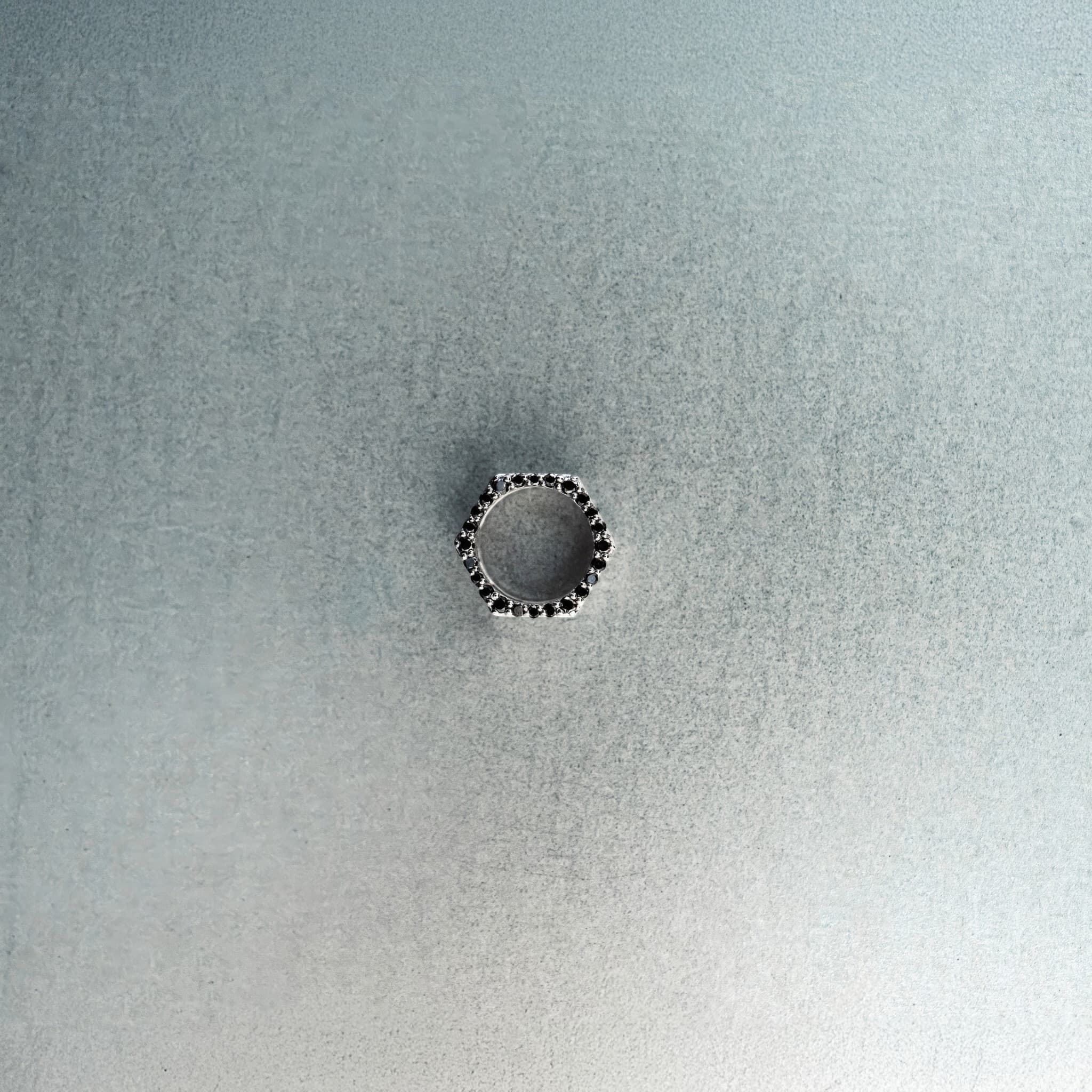 Silver hex nut bead with black diamond detailing on light gray surface