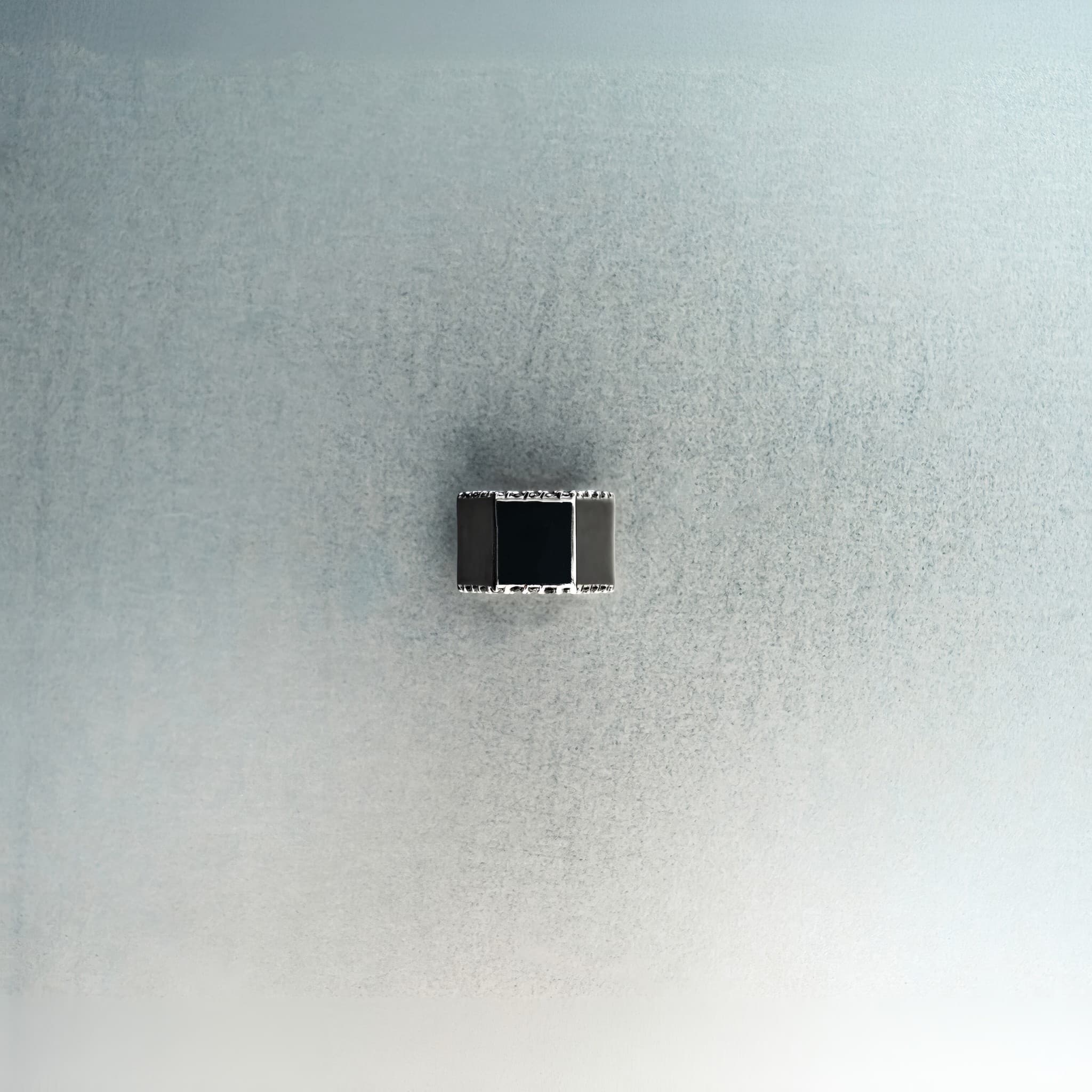 Silver hex nut bead with black diamond detailing on light gray surface