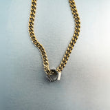 Gold chain necklace with silver hex nut bead featuring black diamond detailing on light gray surface
