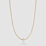 A delicate gold ball chain necklace with a small, polished silver hexagonal pendant, displayed against a light gray background.