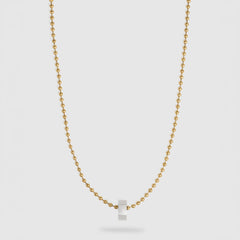 A delicate gold ball chain necklace with a small, polished silver hexagonal pendant, displayed against a light gray background.