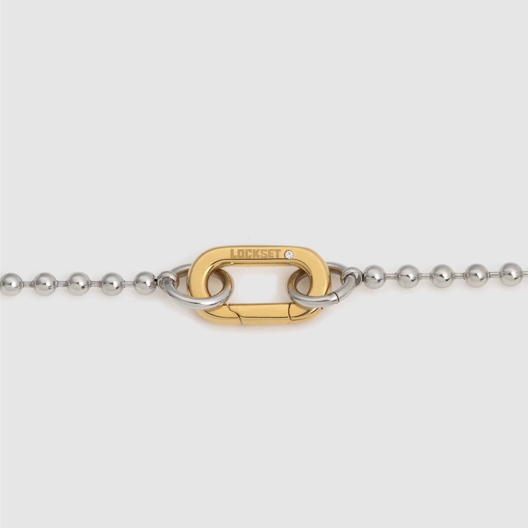 A close-up of a gold and silver interlocking chain link closure, with the brand name 'LOCKSET' engraved on the gold link, set against a light gray background.