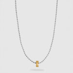 A delicate silver ball chain necklace featuring a small, polished gold hexagonal pendant at the center, displayed against a light gray background.