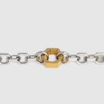 A close-up of a silver-toned metal chain bracelet with a central gold-toned hexagonal clasp, shown against a light gray background.