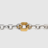A close-up of a silver-toned metal chain bracelet with a central gold-toned hexagonal clasp, shown against a light gray background.