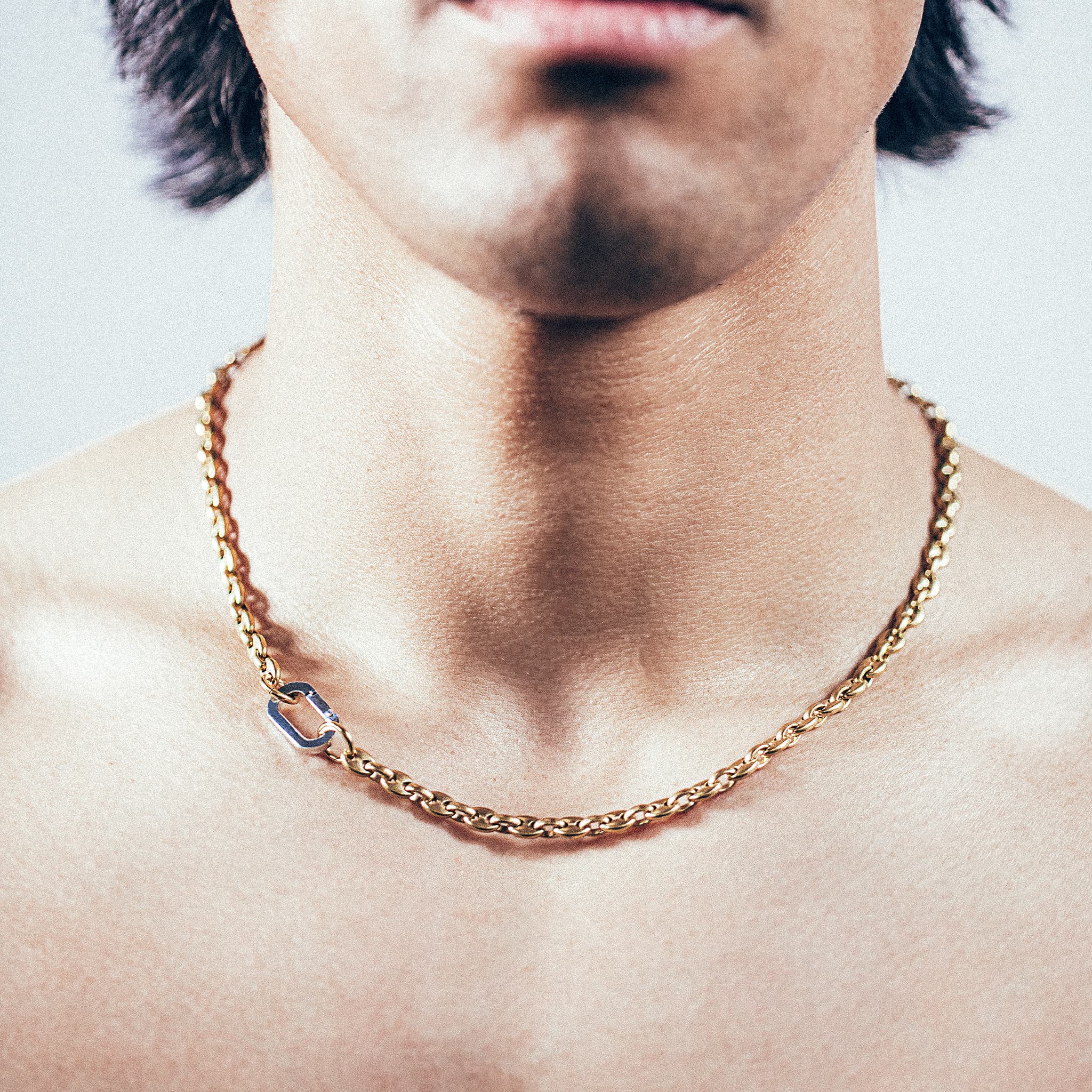 Close-up of man wearing gold mariner chain necklace with silver carabiner clasp