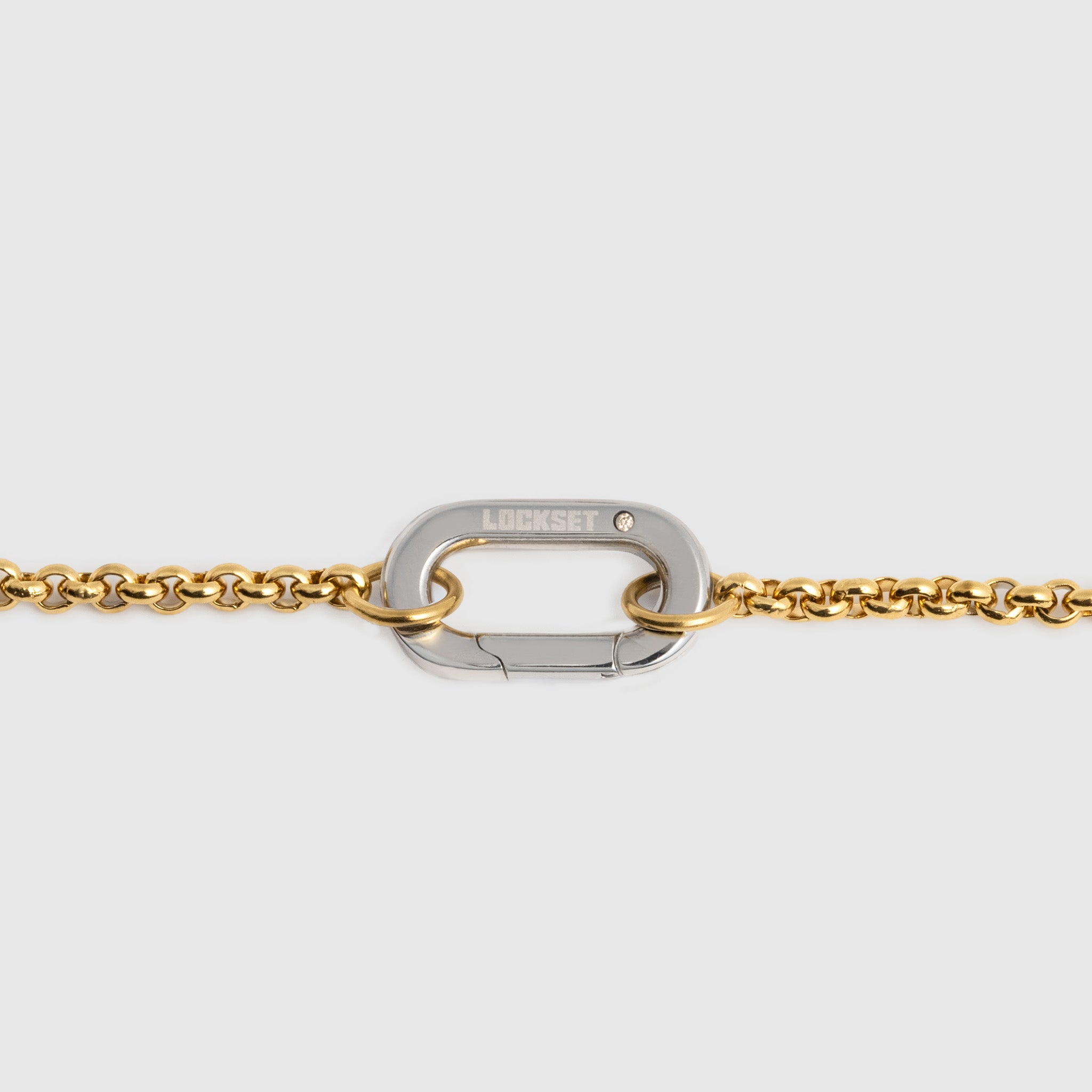 A close-up of a gold chain bracelet featuring a silver-toned carabiner clasp engraved with the brand name 'LOCKSET' on a light gray background.