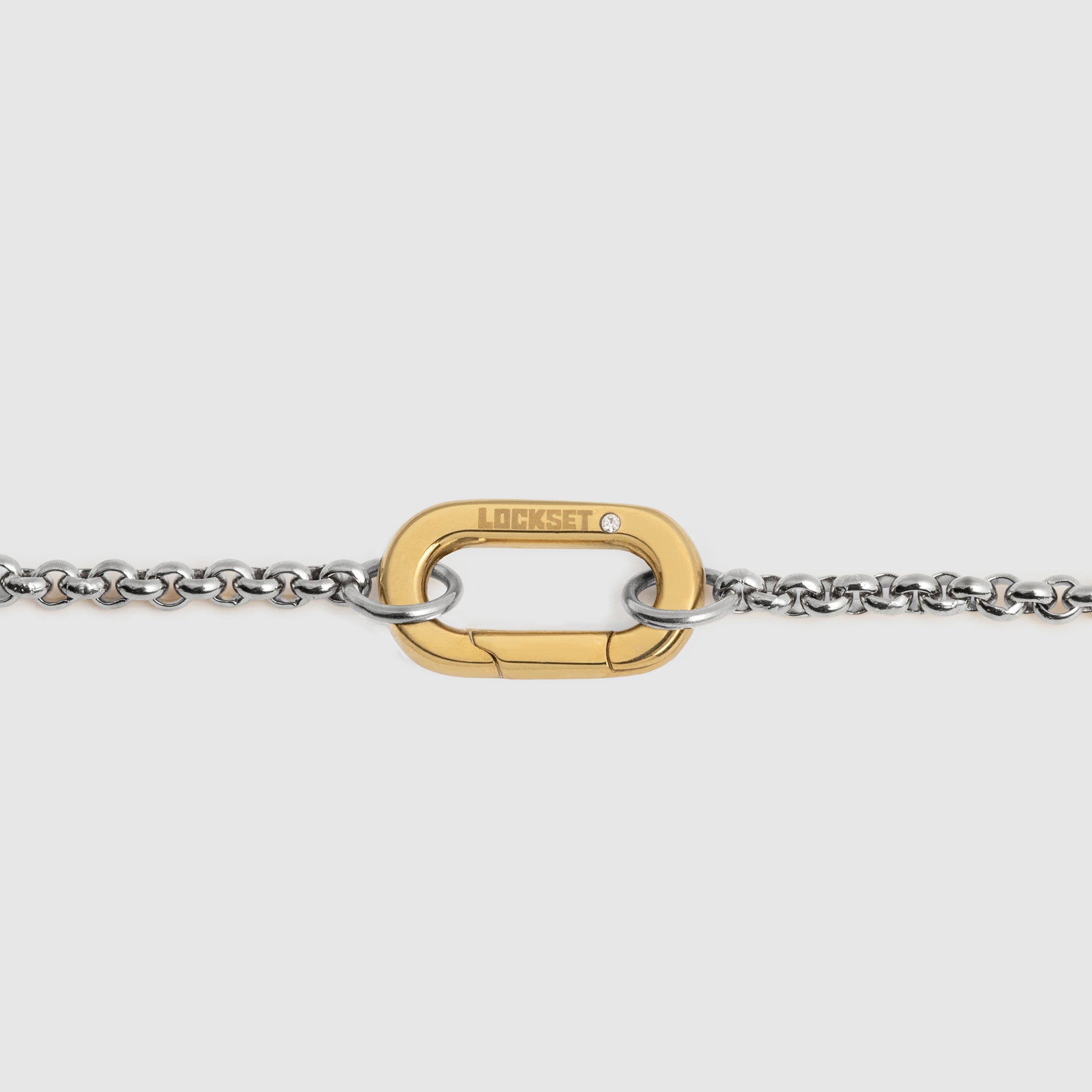 A close-up of a gold-tone carabiner clasp connected to a silver-tone chain, shown against a light gray background. The brand name 'LOCKSET' is engraved on the gold clasp.