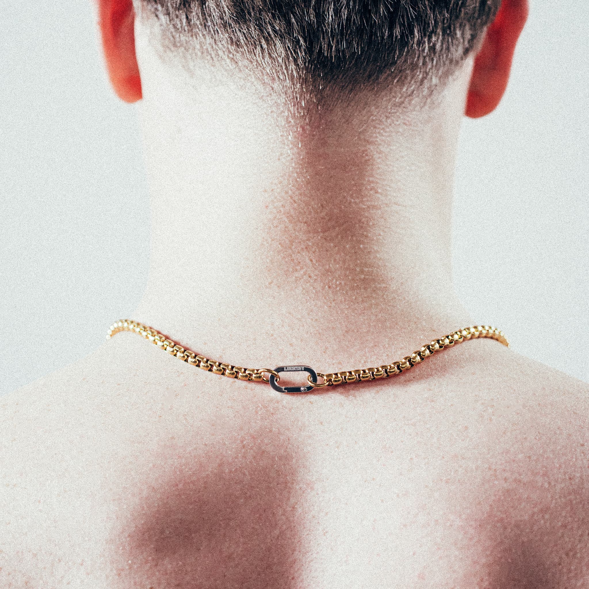 Close-up of man wearing thick gold rolo chain necklace with silver carabiner clasp