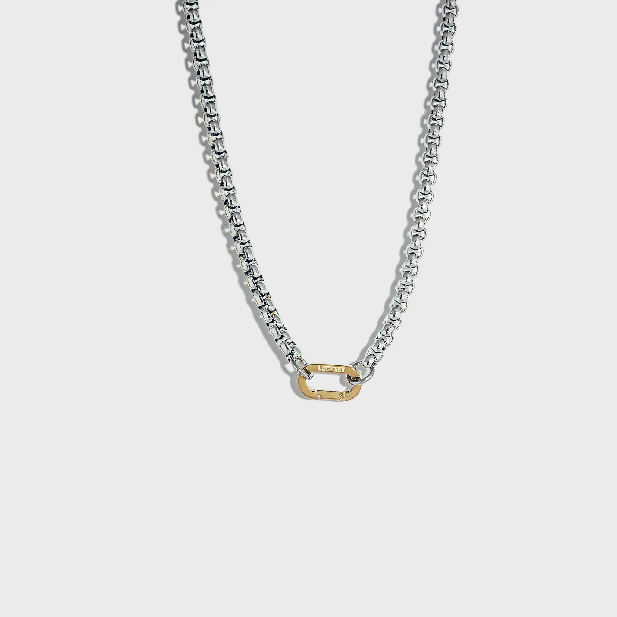 Thick silver rolo chain necklace with gold carabiner clasp on white background