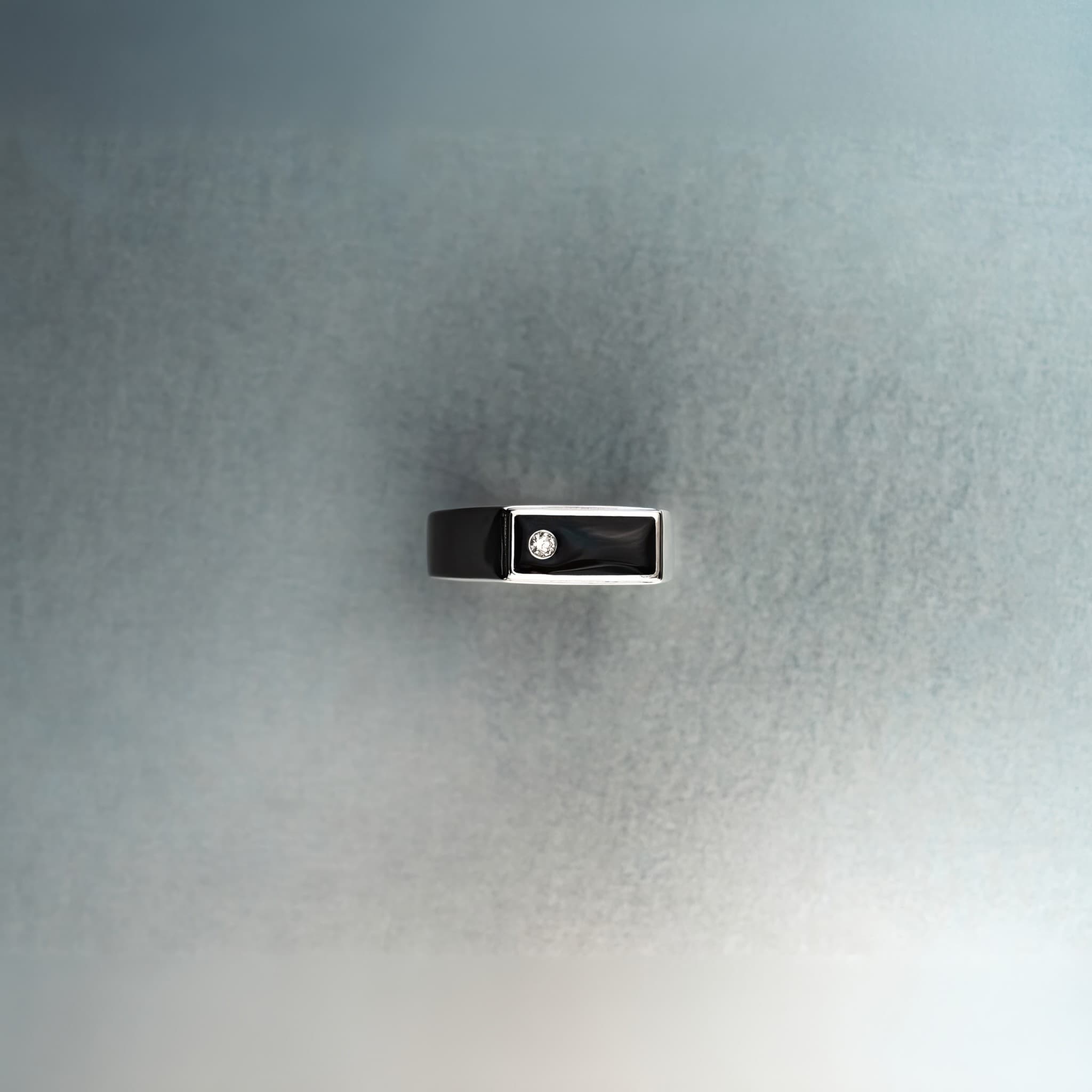 Black and silver rectangular signet-style ring with diamond detail on textured gray background