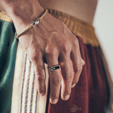 Hand wearing gold bracelet and rectangular signet-style ring with diamond detail on textured fabric background