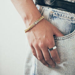 Close-up of hand wearing gold bracelet and silver  ring on textured fabric background