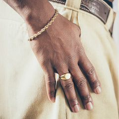 Hand wearing gold bracelet and round gold signet ring on textured fabric background