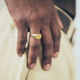 Close-up of hand wearing gold round signet ring on textured fabric background