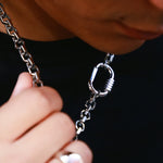 A close-up lifestyle shot of a person wearing a silver chain necklace with a carabiner clasp, holding the chain near their neck against a black background.