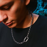 A close-up lifestyle shot of a man wearing a silver chain necklace with a carabiner clasp, paired with a black t-shirt.